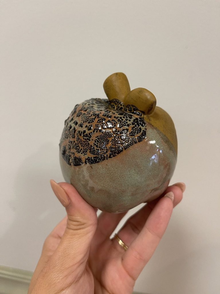 Hand-painted apple with a gray-green body and black crackle glaze top, held in hand