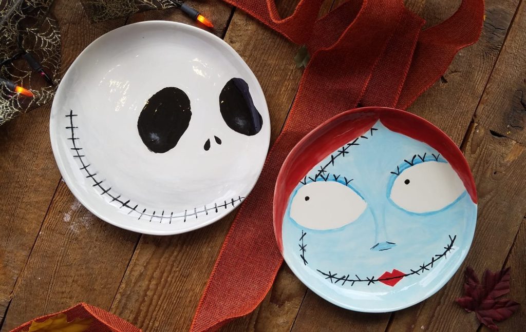 Two hand-painted round plates with Jack Skellington and Sally faces on a rustic table