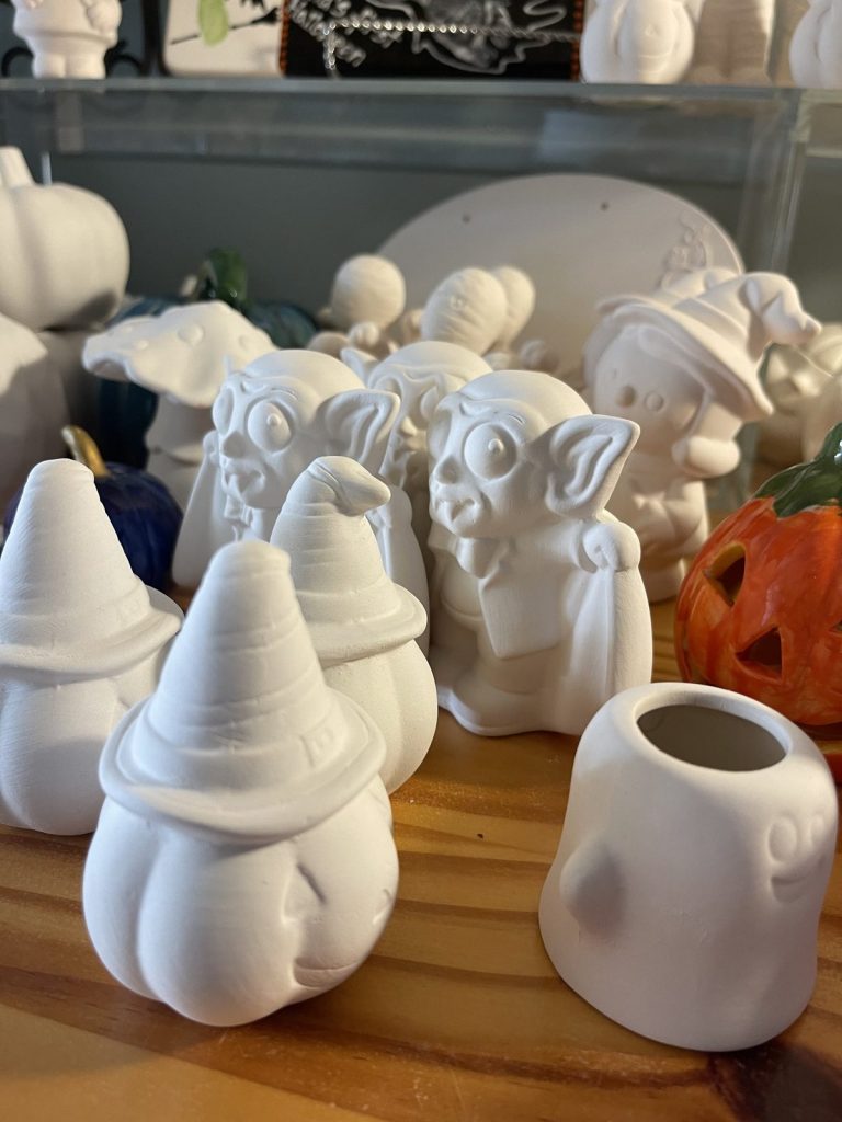 Unpainted white bisque gnomes, ghosts, and Halloween figurines waiting on a studio shelf