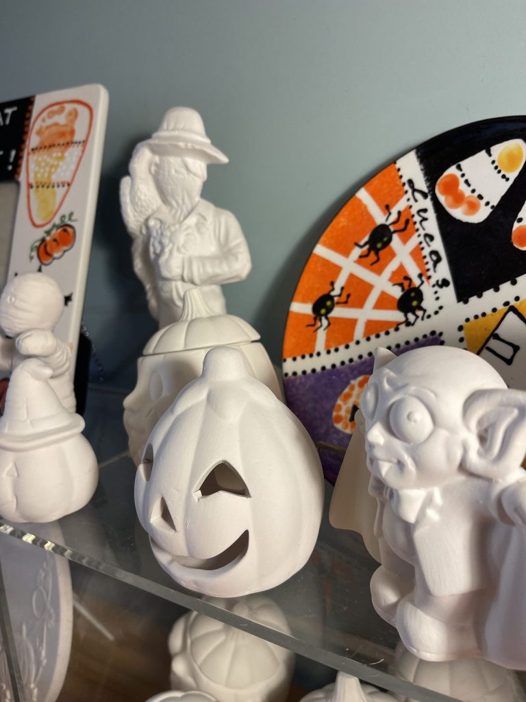Unpainted bisque jack-o'-lantern and figurines beside a hand-painted candy corn and spiderweb platter