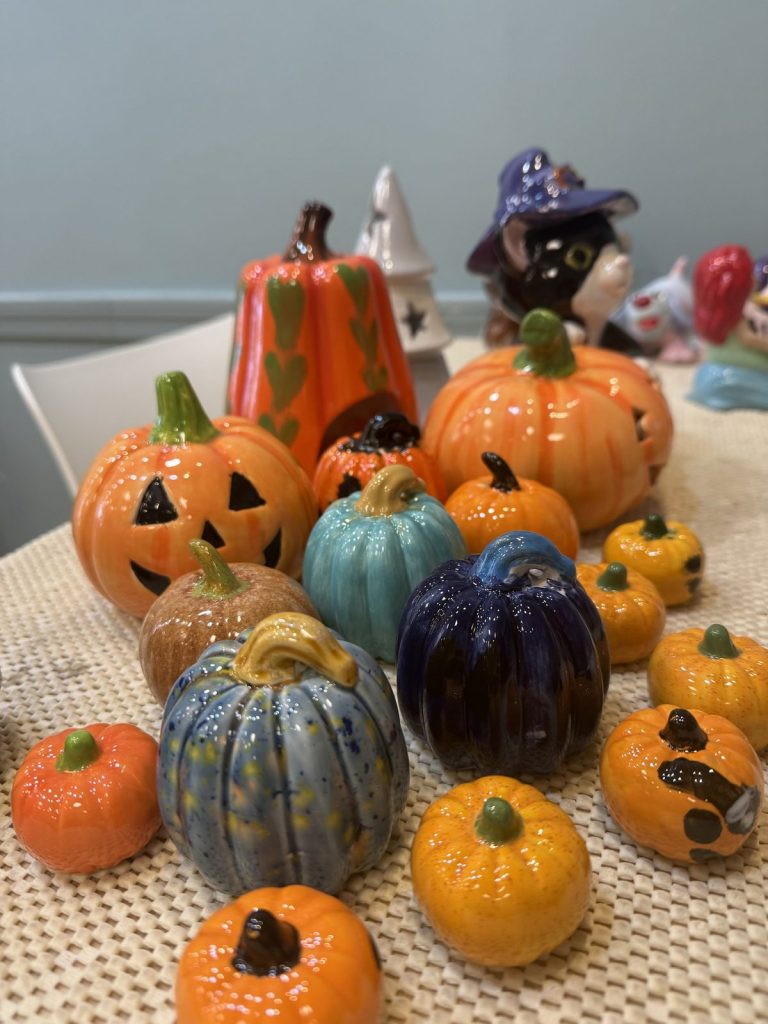 Table of hand-painted pumpkins and jack-o'-lanterns in orange, teal, and blue