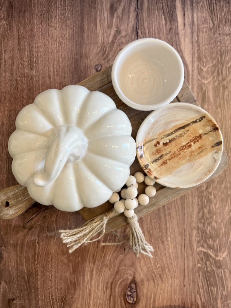 Hand-painted white pumpkin with a twisted stem beside two small bowls on a wooden board