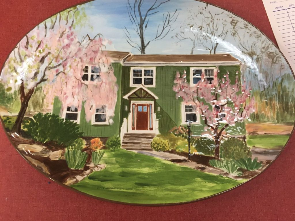 Hand-painted oval platter of a green house framed by blossoming pink spring trees