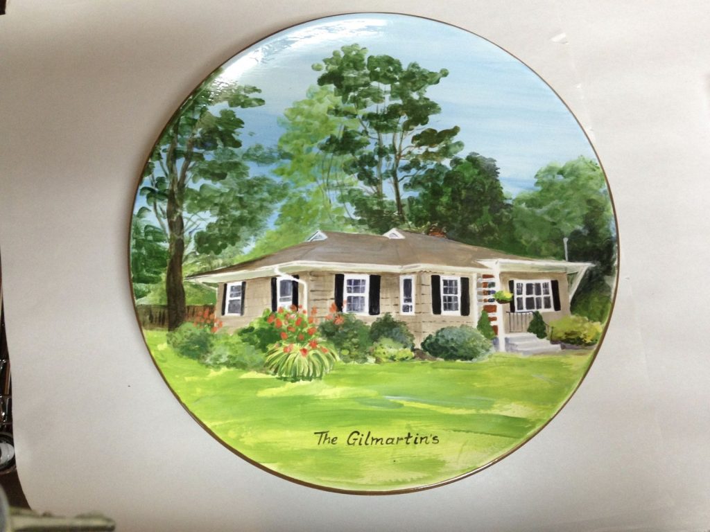 Hand-painted round plate of a tan ranch house with black shutters and a green lawn