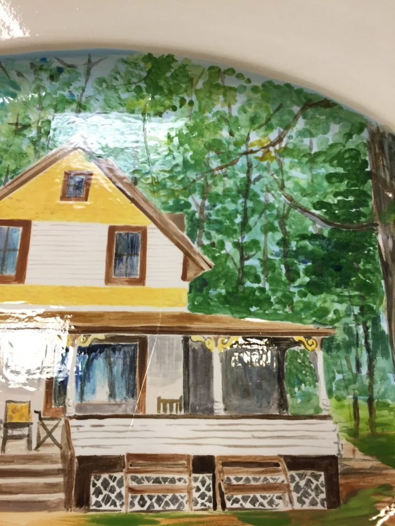 Hand-painted platter detail of a yellow and white house with a covered porch among green trees