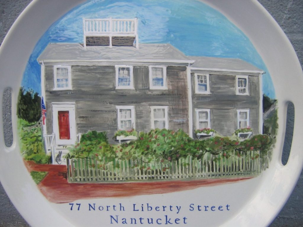 Close-up of a hand-painted gray shingled Nantucket house with a red door and picket fence