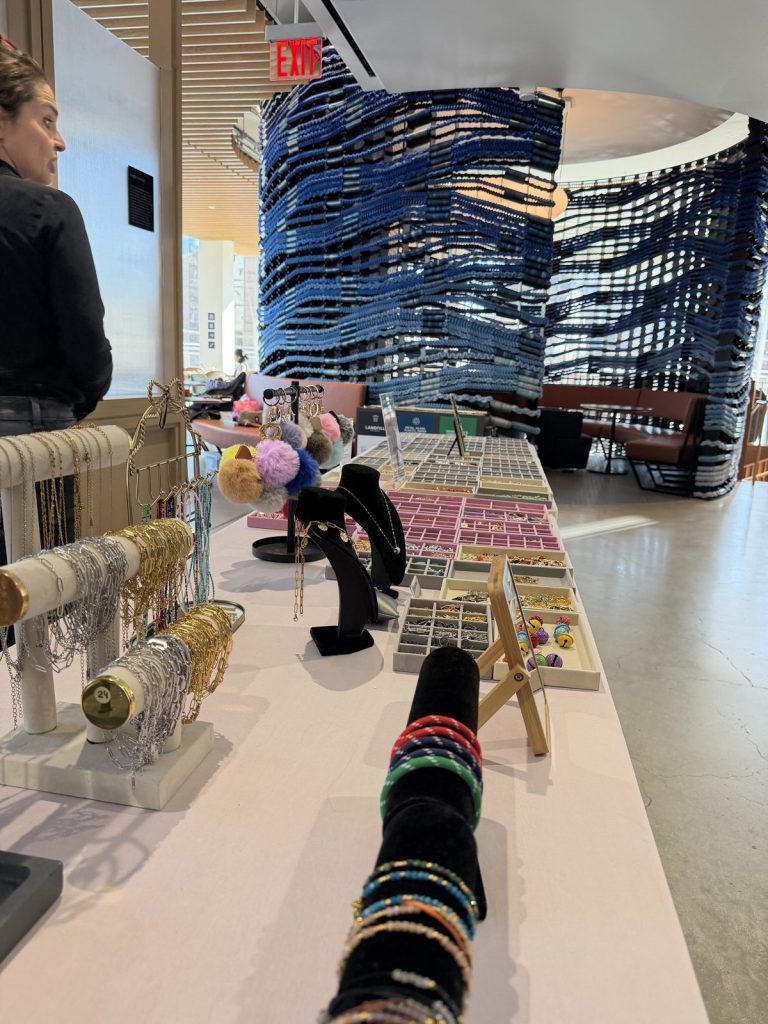 Bracelet stands, necklace busts and charm trays along a Mobile Charm Bar table at an office event