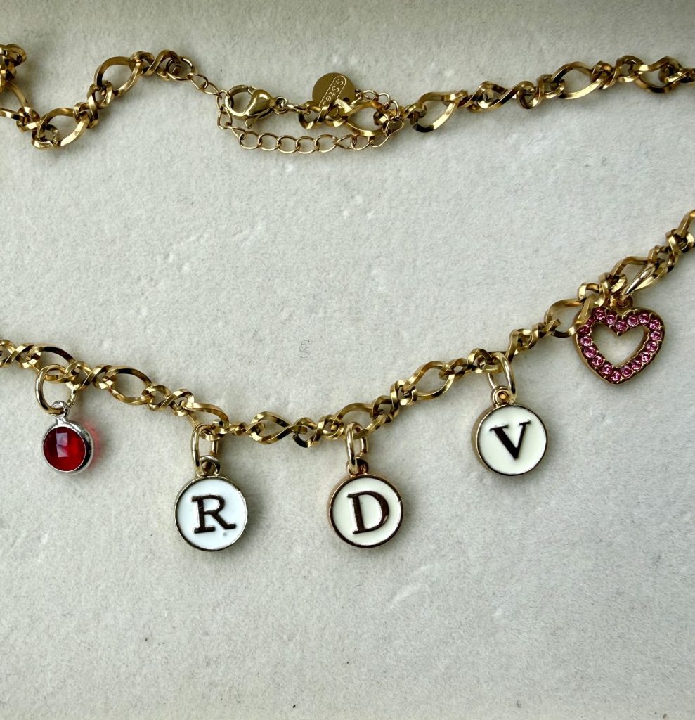 Gold chain with letter charms R, D and V, a red stone and a pink heart