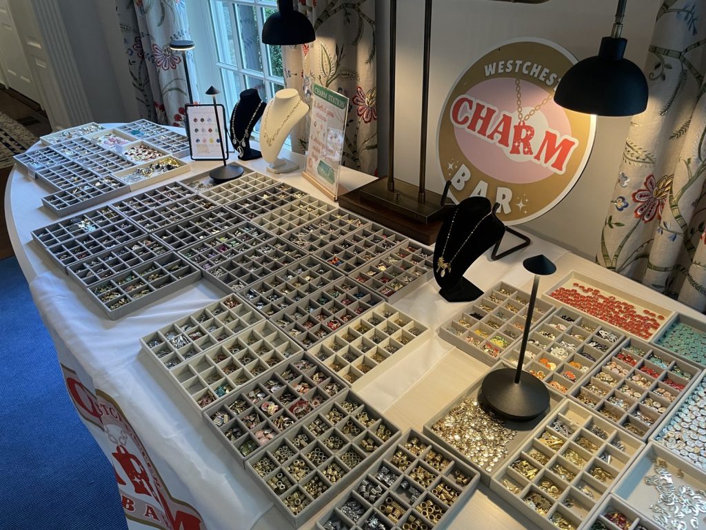 Charm trays and necklace displays beside the Westchester Charm Bar sign