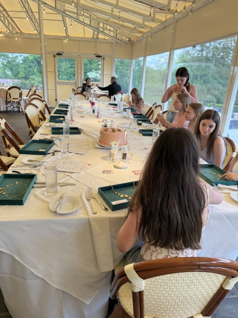 Guests making charm jewelry at a long luncheon table in a sunroom