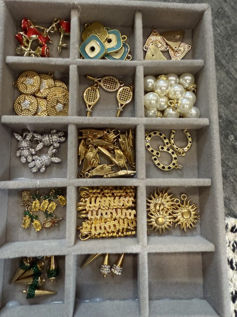 Tray of gold charms: tennis rackets, pearls, suns and more