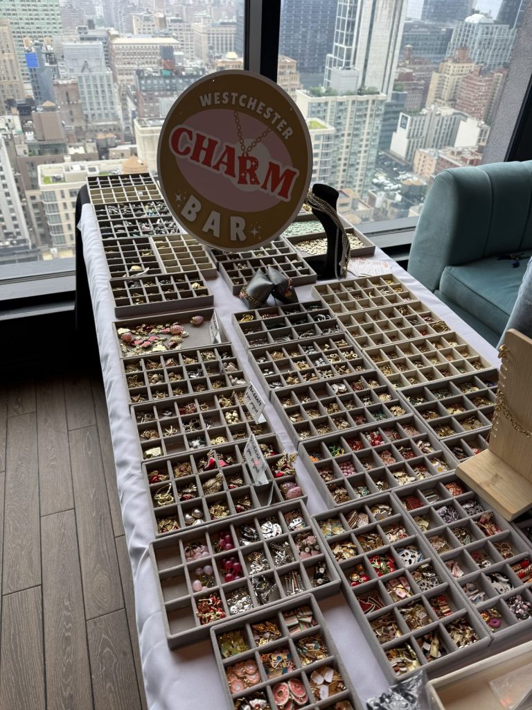 The Westchester Charm Bar sign and trays of charms beside a velvet sofa at a private event