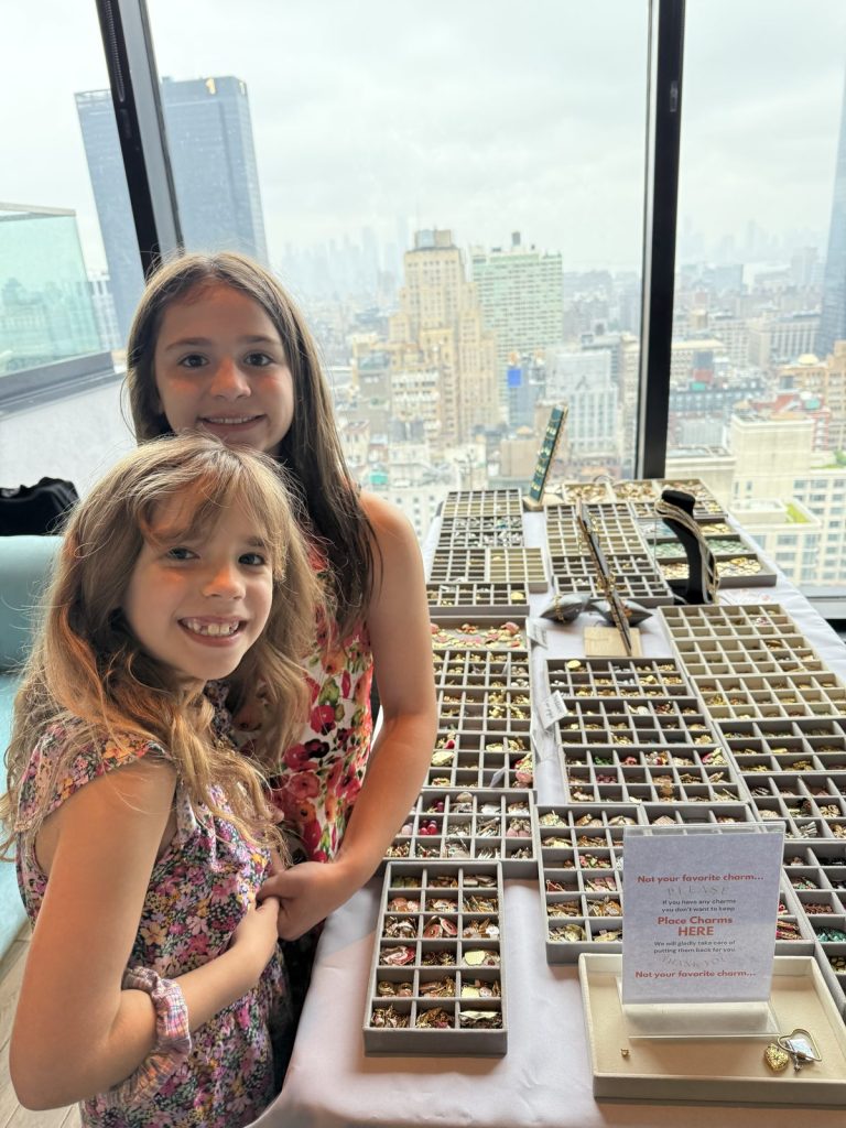 Two smiling girls at the Mobile Charm Bar with the city behind them
