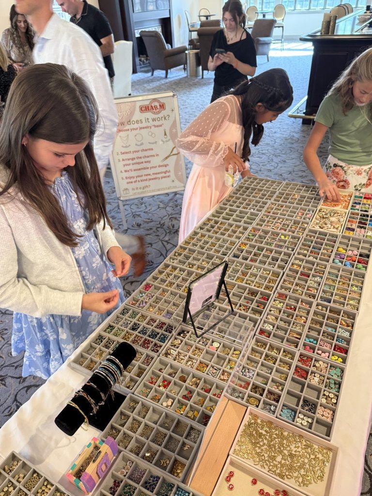 Girls choosing charms at a long Charm Bar table