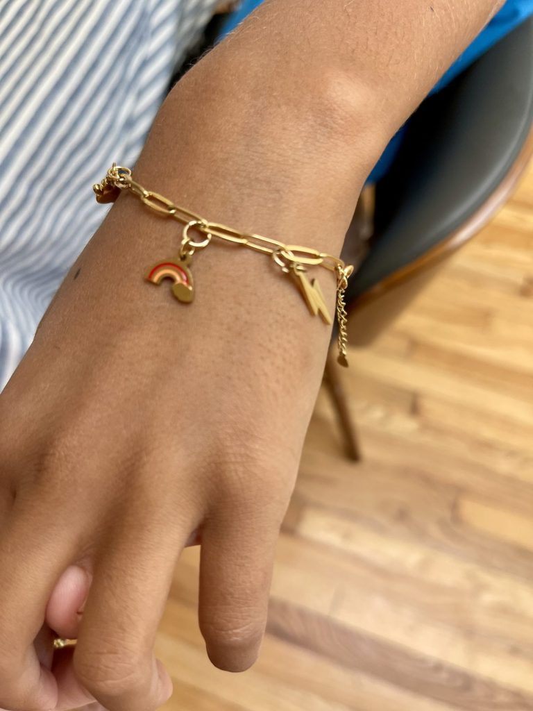 A child wearing a gold charm bracelet with a rainbow charm