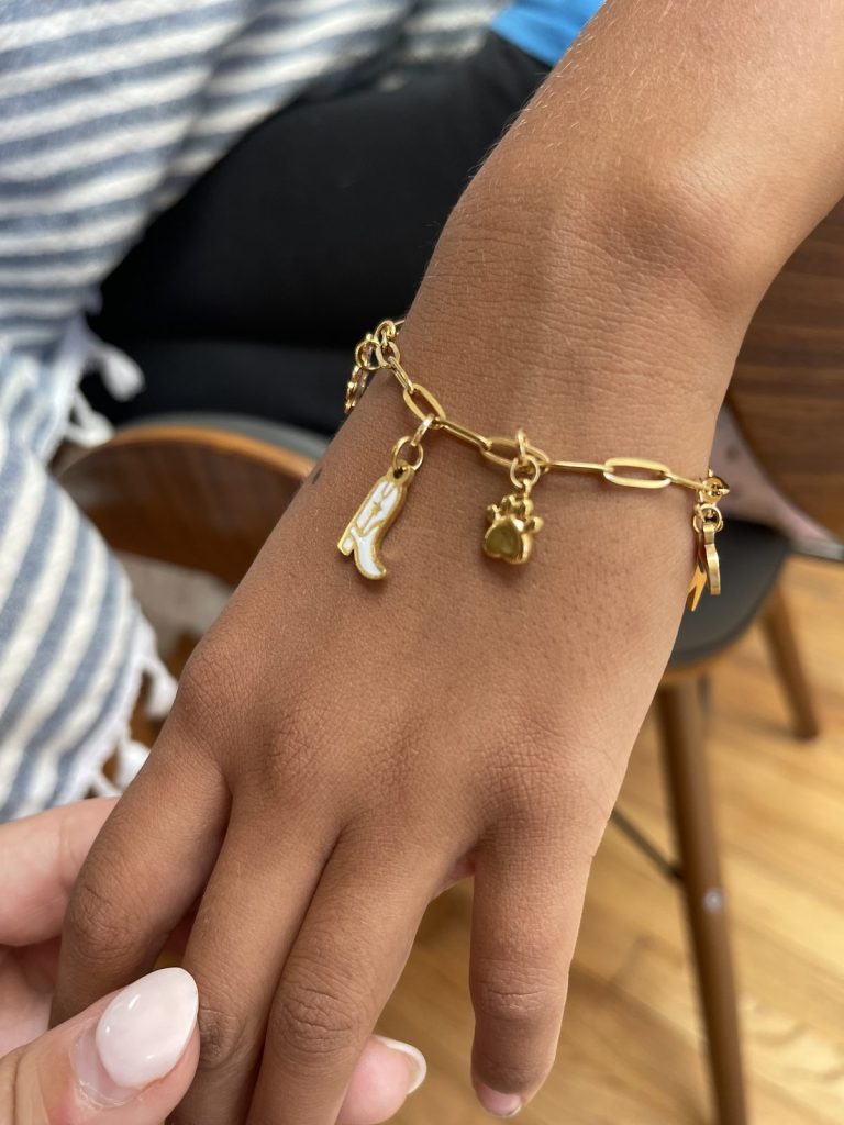 A gold charm bracelet with a boot charm on a guest's wrist