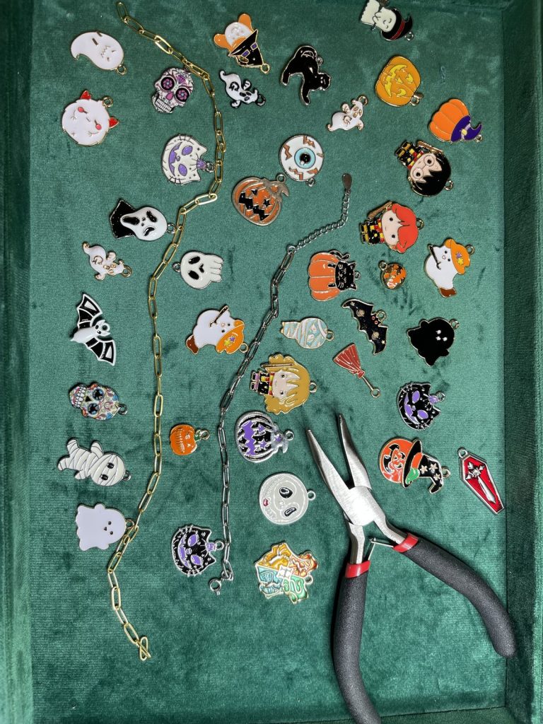 Halloween charms laid out on green velvet with jewelry pliers