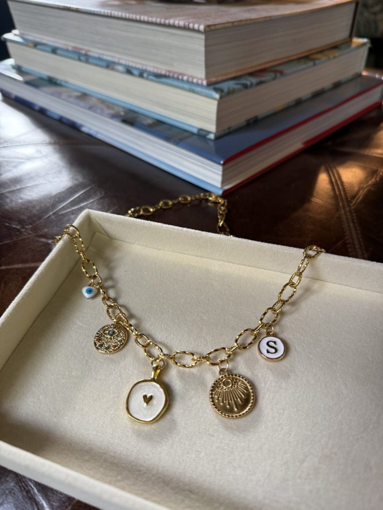 Gold charm necklace with an initial S and medallion charms in a gift box