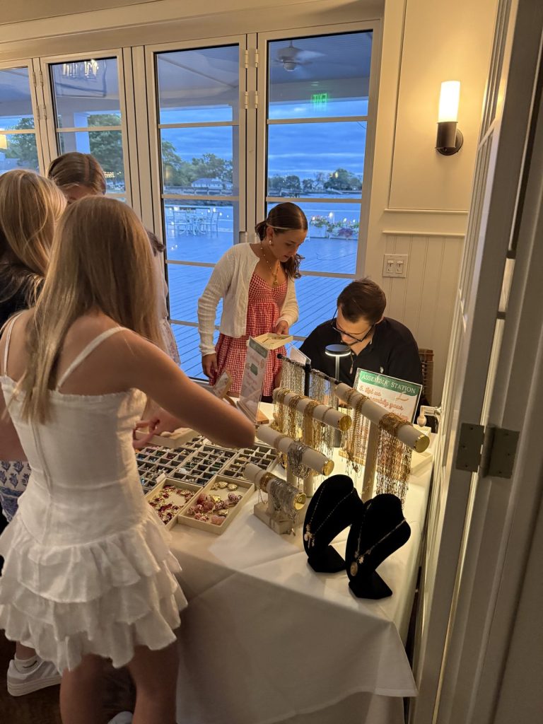 Guests choosing charms at a Mobile Charm Bar table by the water at an evening event