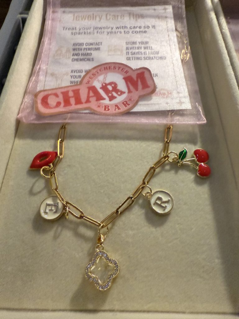 Charm necklace with initials, red lips, cherries and a crystal clover, on a Westchester Charm Bar pouch