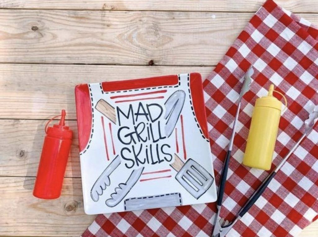 Square Mad Grill Skills plate painted like a grilling apron with tongs and spatula