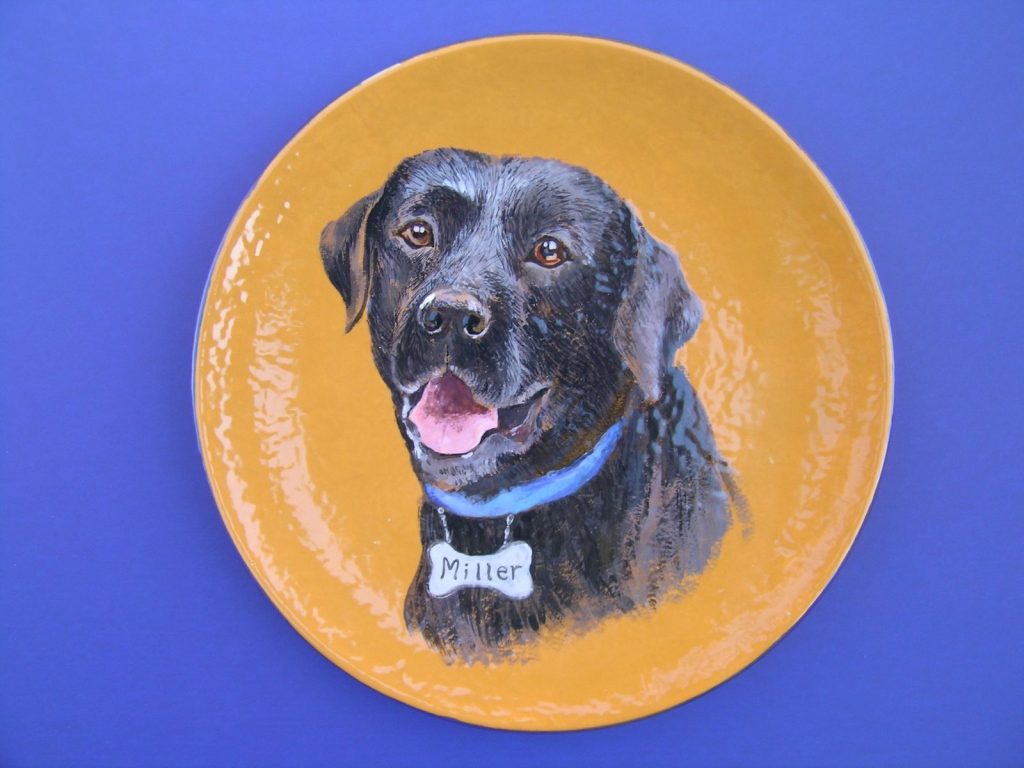 Hand-painted round plate portrait of a black Labrador with blue collar and bone tag on gold
