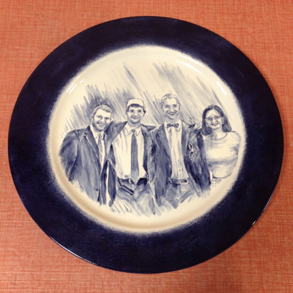 Hand-painted blue and white family portrait plate of four smiling adults with a deep cobalt rim