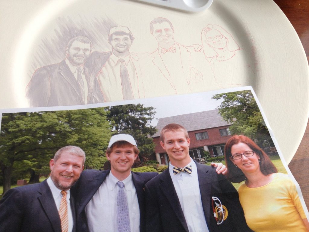 Penciled family portrait sketch on a plate beside the reference photo of four smiling adults
