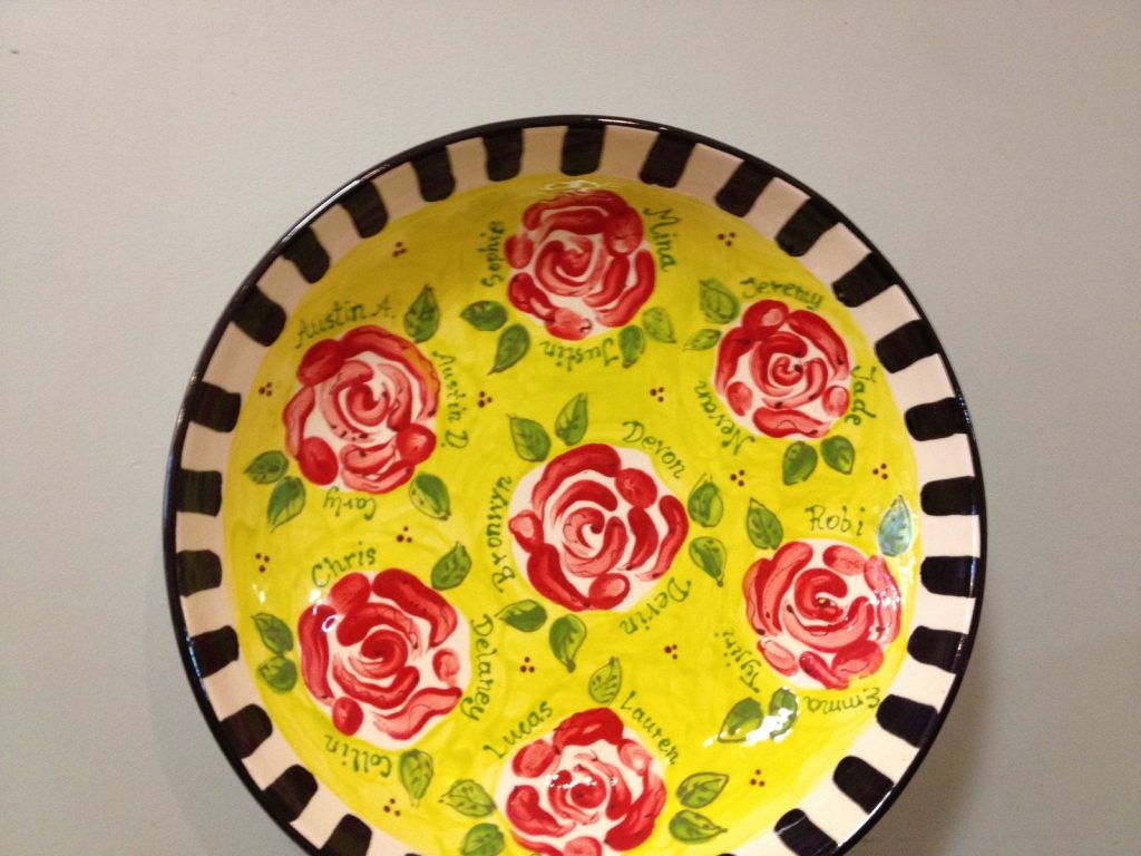 Yellow bowl with a black-and-white striped rim and red painted roses labeled with students' names