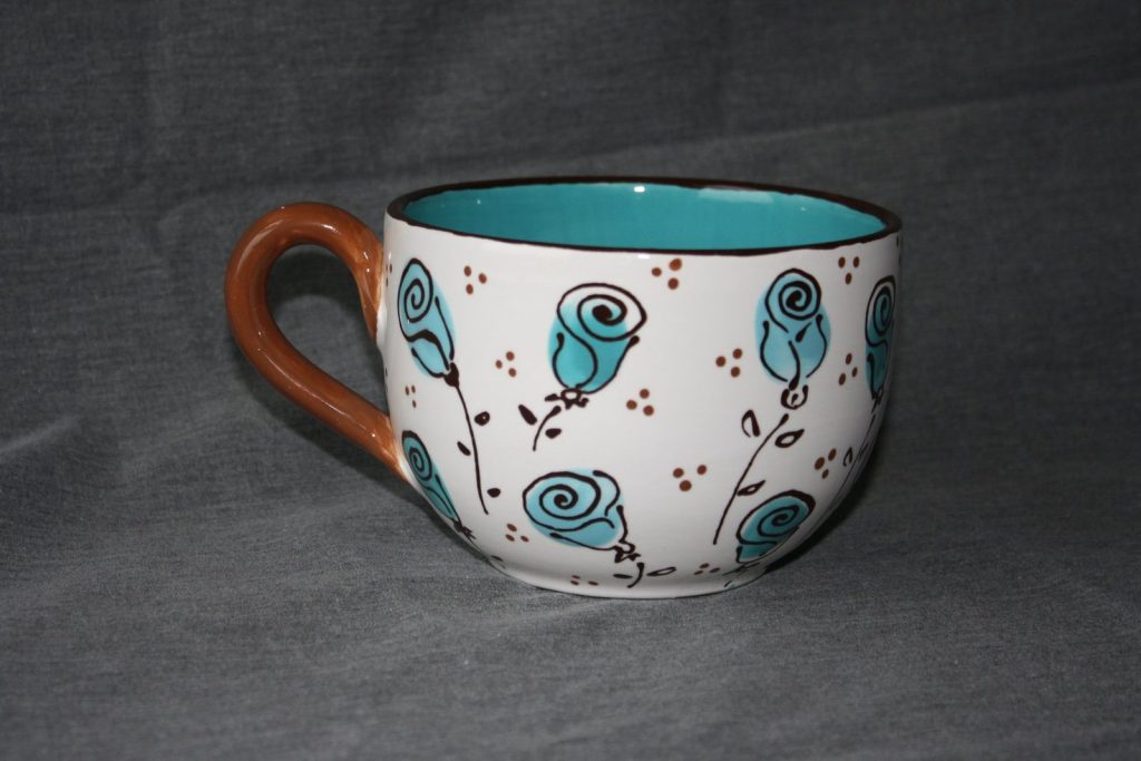 Hand-painted oversized mug with teal swirl roses and red dots on white with an orange handle