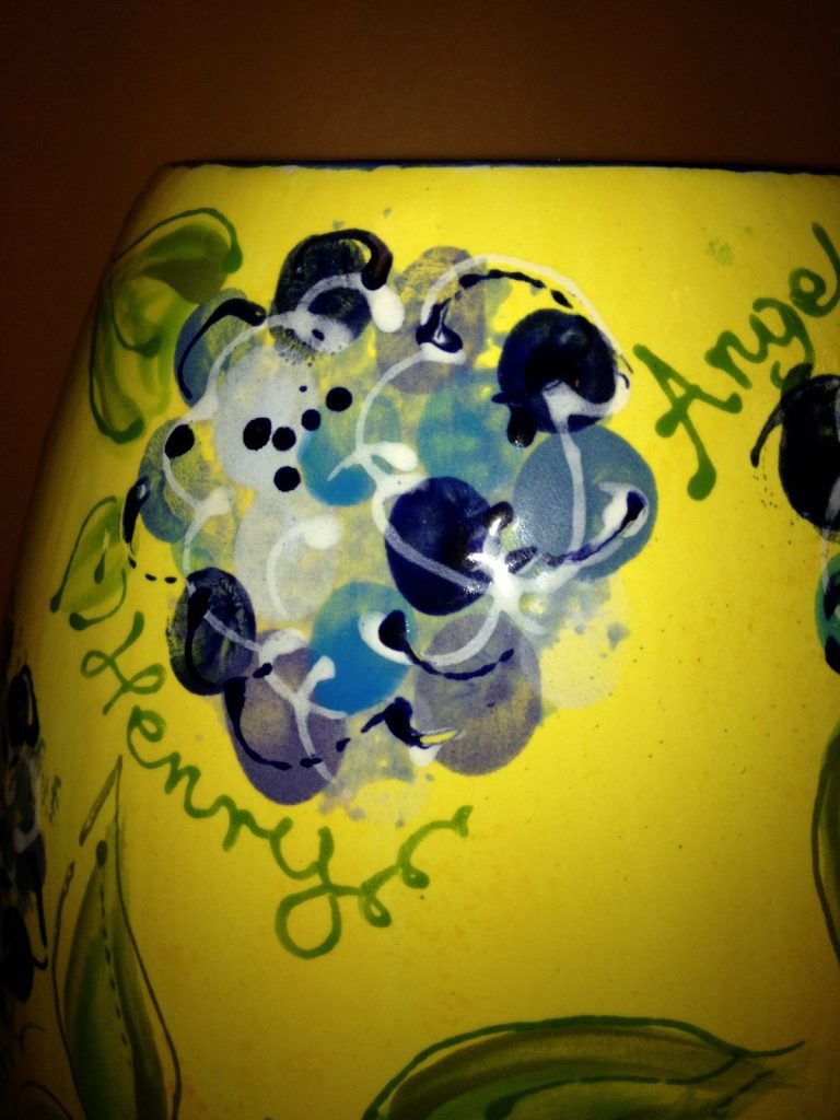 Close-up of a hand-painted yellow vase with a blue fingerprint hydrangea and handwritten names