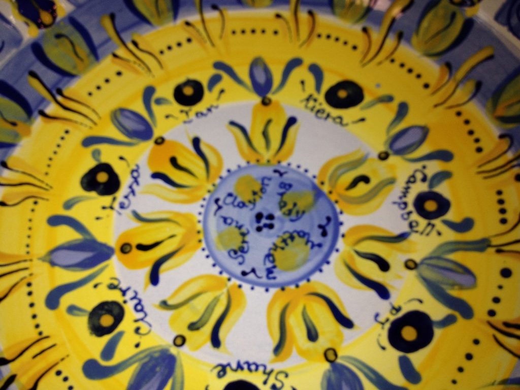 Close-up of a hand-painted yellow and blue Tuscan-style platter with olive motifs and children's names