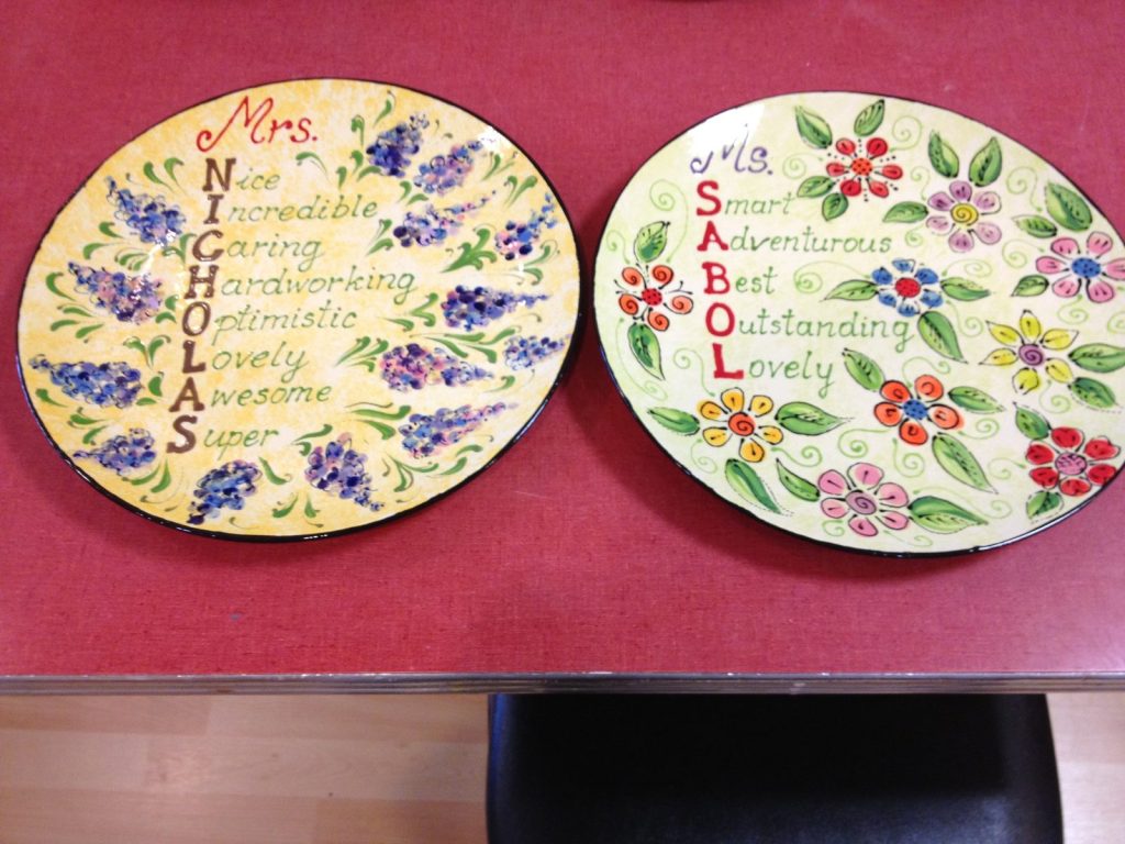 Two hand-painted teacher plates with acrostic name poems framed by purple and colorful flowers