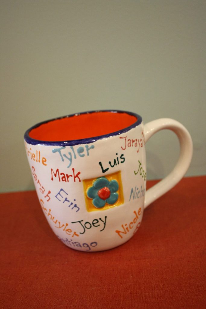 Hand-painted mug with an orange interior, a flower center and children's names in colorful lettering