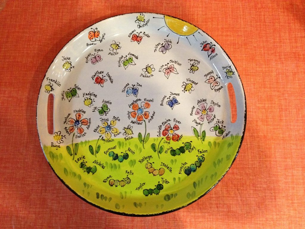 Hand-painted round handled platter of fingerprint flowers in a green meadow under a smiling sun