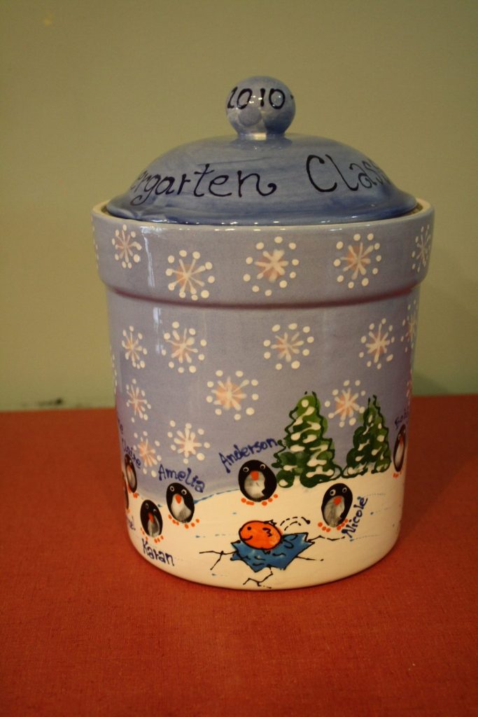 Reverse side of a hand-painted snowy kindergarten canister with fingerprint penguins and a sledding child