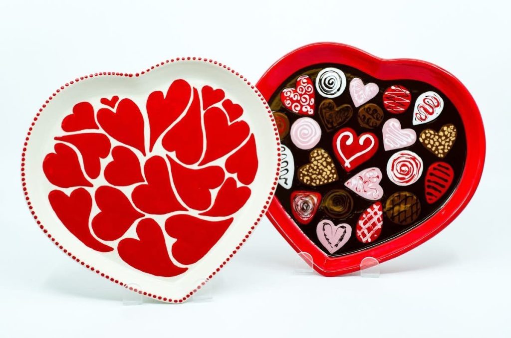 Two hand-painted heart plates, one covered in red hearts, one painted as a chocolate box