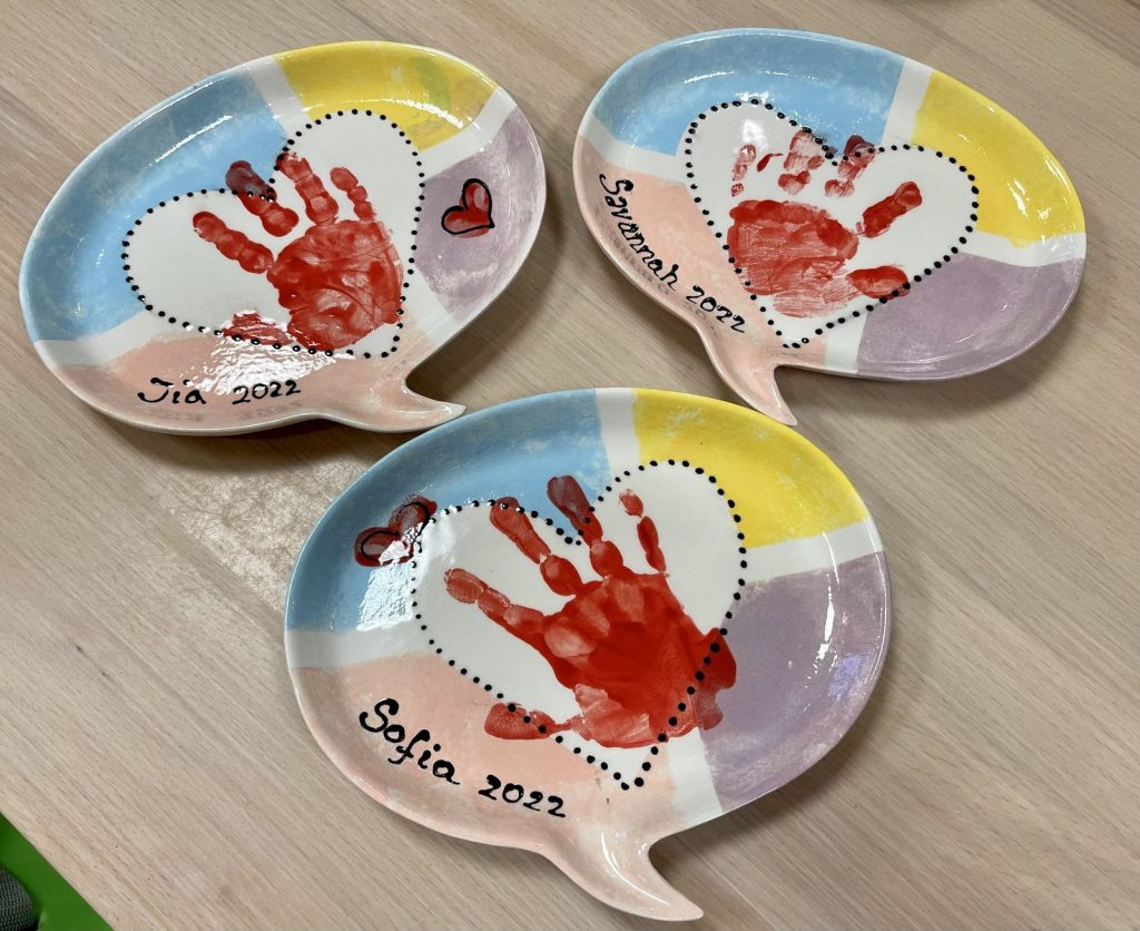 Three speech-bubble dishes with red handprint hearts in pastel color blocks, each with a first name
