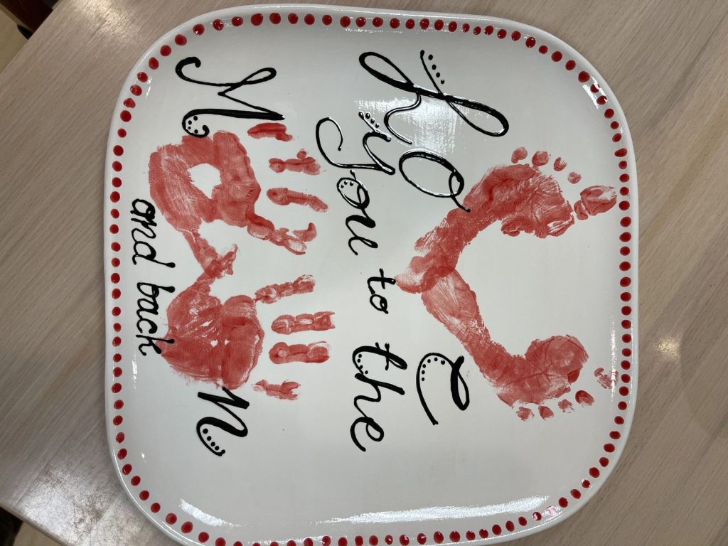 Square plate with red handprints and footprints reading Love You to the Moon and Back