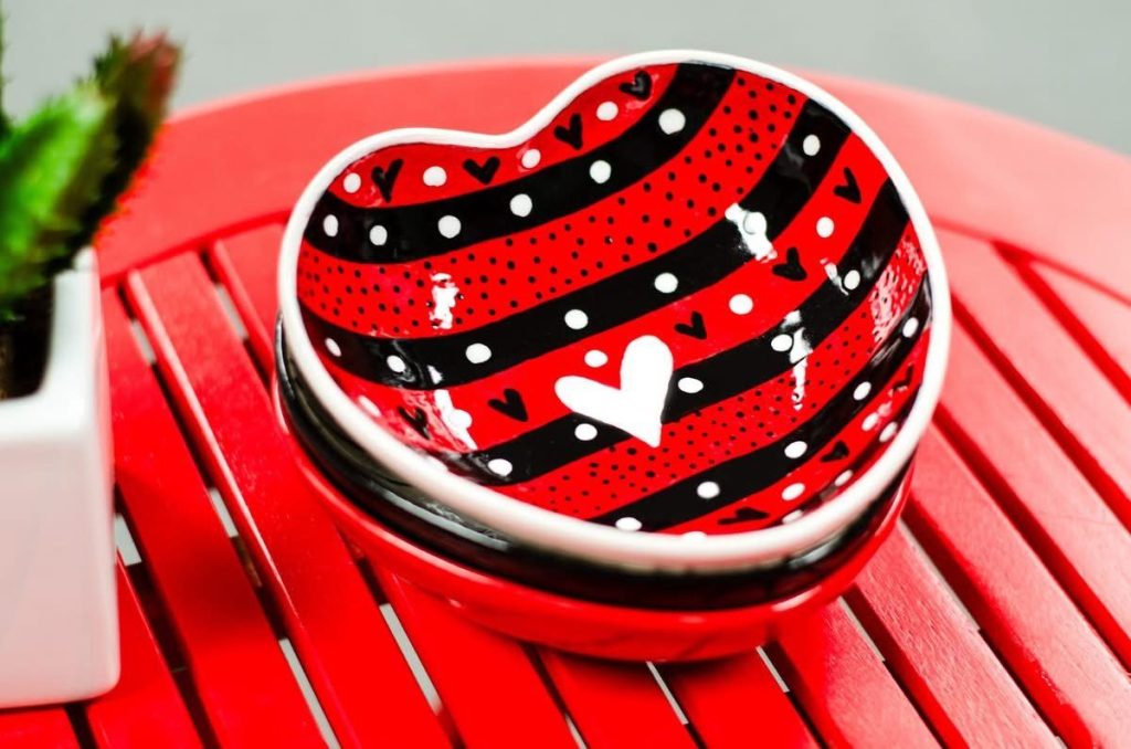 Heart-shaped bowl hand-painted with red and black stripes, polka dots and a white heart
