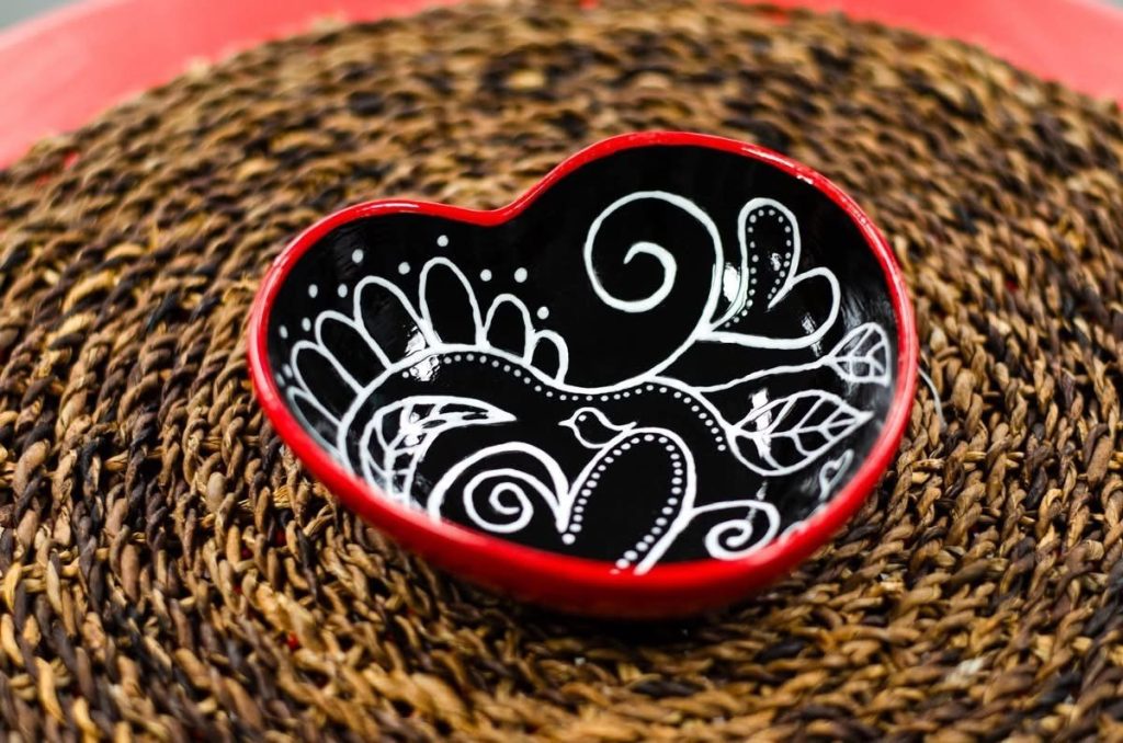 Black heart-shaped bowl with red rim, painted with white swirling bird and leaf designs