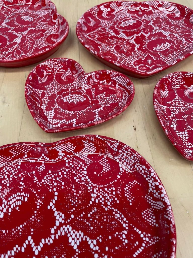 Several red heart-shaped plates textured with a white lace pattern