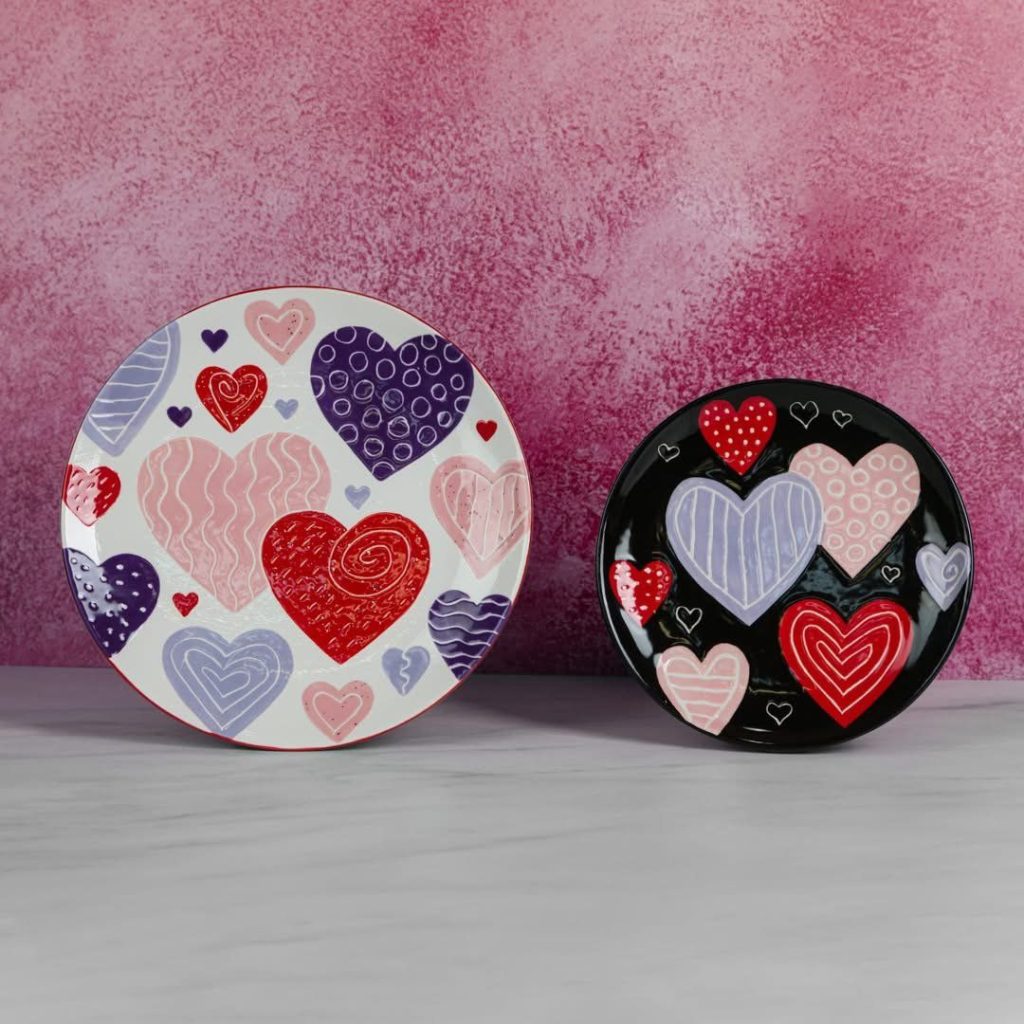 Two round plates, one white and one black, painted with pink, purple and red hearts
