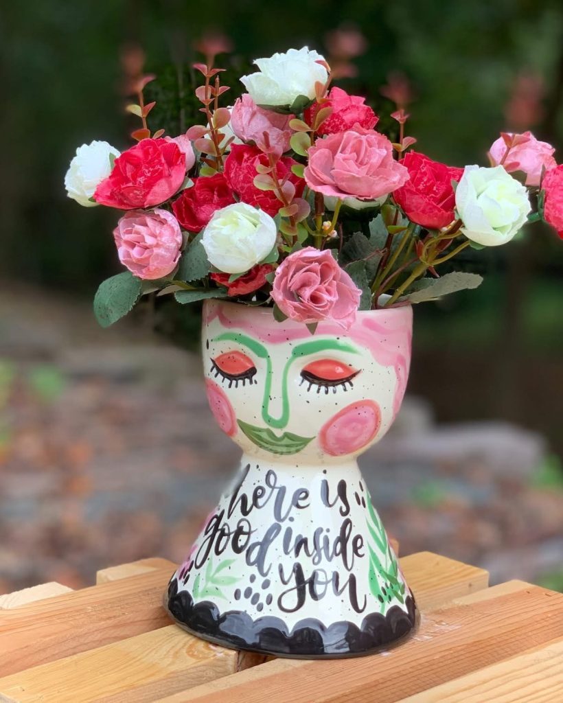 Hand-painted face vase with pink cheeks and the words There Is Good Inside You, holding roses