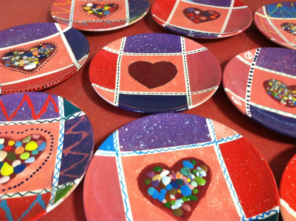 Several hand-painted plates with red and purple quilt-style patches and confetti-filled hearts