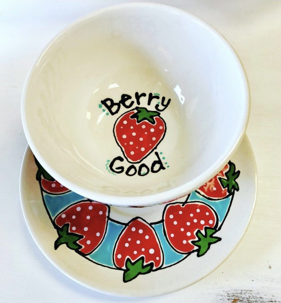 Hand-painted bowl reading Berry Good set on a plate with a border of red strawberries