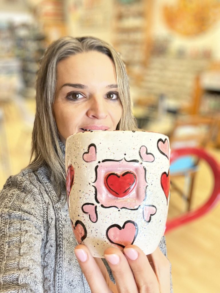 Hand-painted white mug with pink and red hearts around a framed heart center, held up close