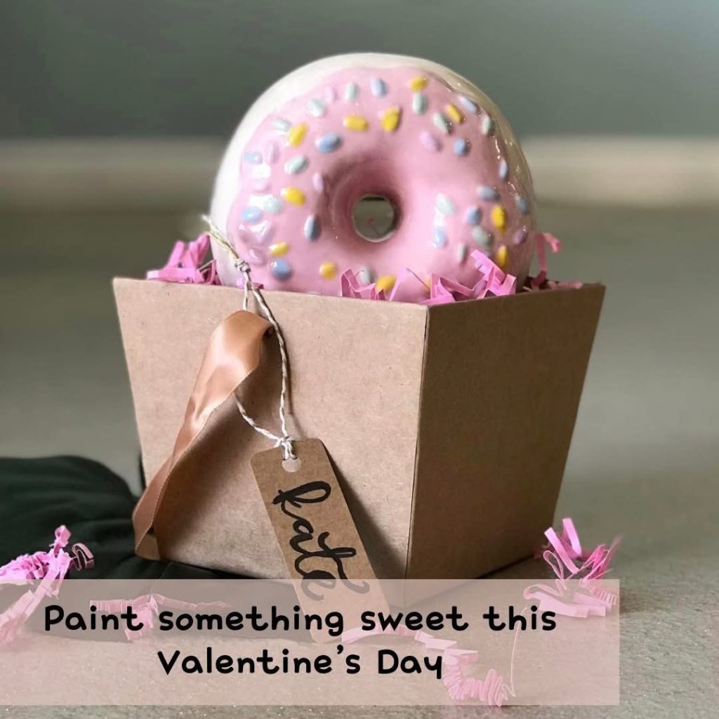 Hand-painted pink-frosted donut with rainbow sprinkles in a kraft gift box with a tag