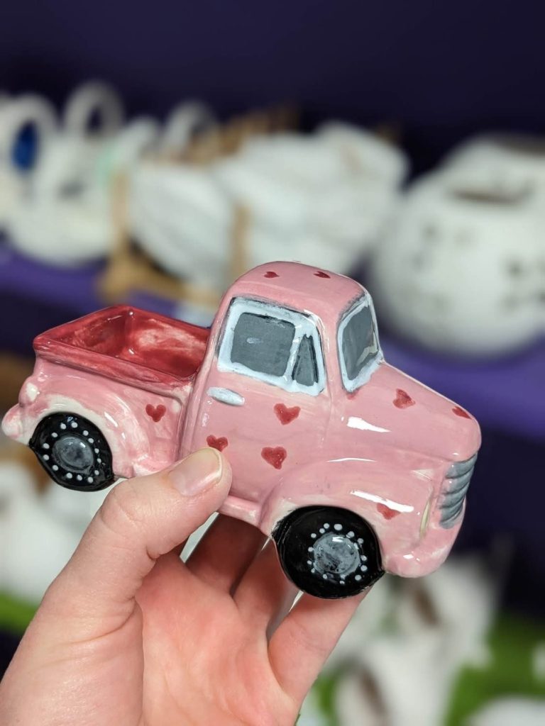 Hand-painted pink vintage pickup truck with red hearts and black tires, held in hand
