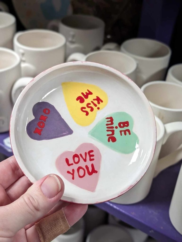 Hand-painted round dish with pastel conversation hearts reading Love You, Be Mine, Kiss Me, and XOXO